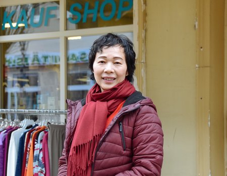 Eine Frau steht vor ihrem Laden und schaut in die Kamera.
