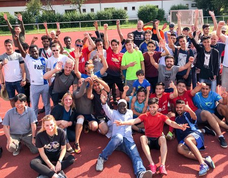 Am Ende waren sie alle Sieger: die Mitpielenden und das Organisationsteam haben sich zum Abschluss für ein Foto im Halbkreis aufgestellt. Die Sieger, das Team Afghanistan, halten stolz ihren Pokal in den Händen. Alle schauen geschafft aber glücklich in die Kamera.