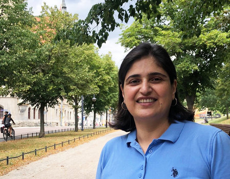 Eine Frau steht in einem Park. Sie trägt ein blaues Poloshirt.