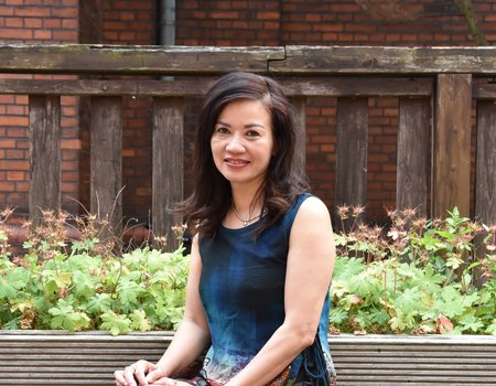 Eine asiatische Frau sitzt auf einer Bank. Sie trägt ein Sommerkleid.