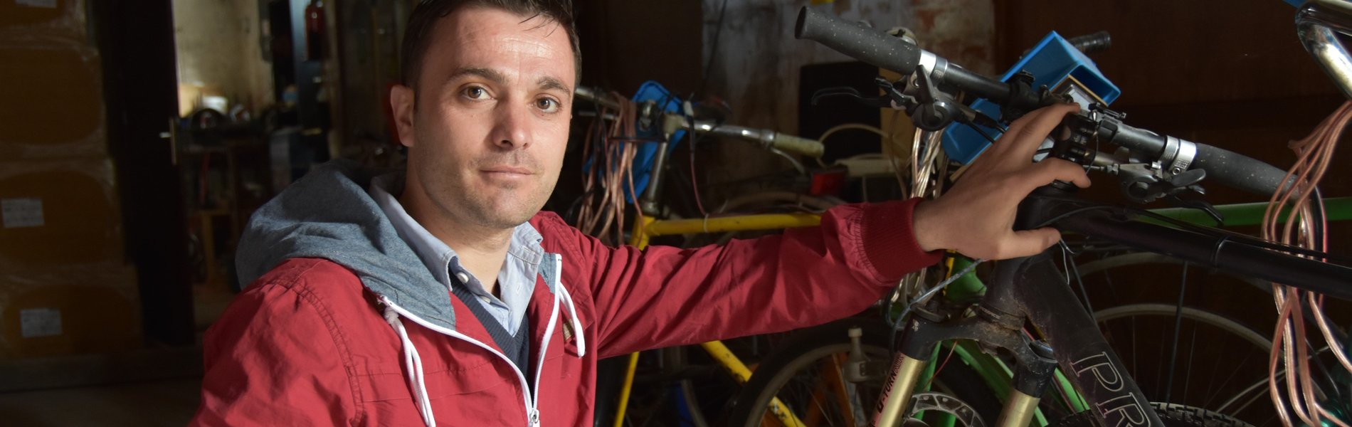 Ein junger Mann mit roter Jacke kniet for einem Fahrrad.