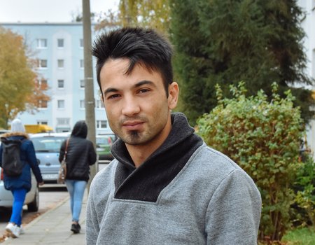 Ein sehr junger Mann aus Syrien steht vor einem Wohnblock. Er schaut ernst.