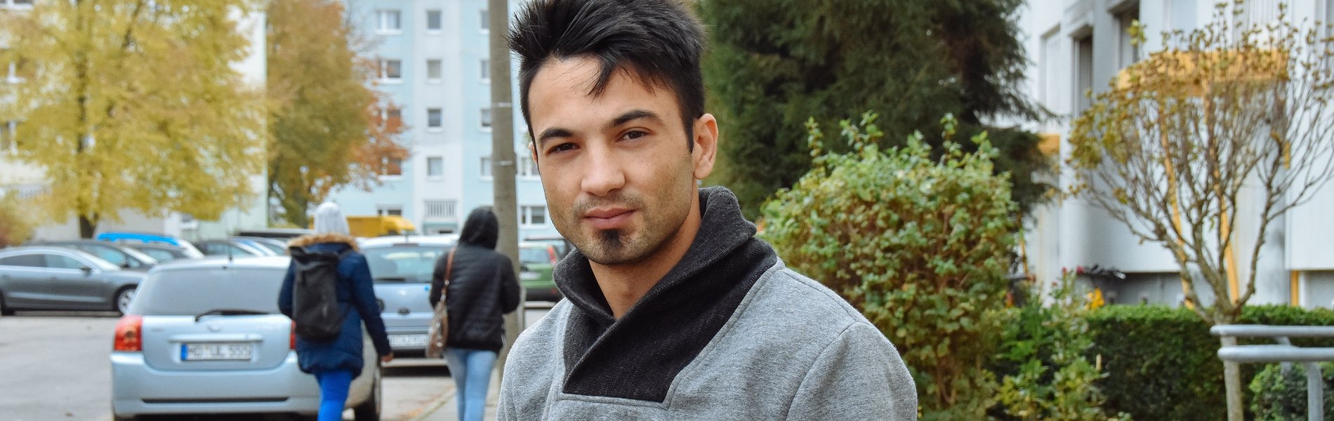 Ein sehr junger Mann aus Syrien steht vor einem Wohnblock. Er schaut ernst.