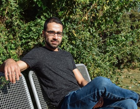 Ein junger Mann sitzt auf einer Parkbank und die Sonne scheint.