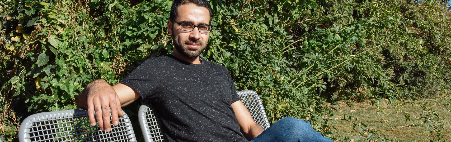Ein junger Mann sitzt auf einer Parkbank und die Sonne scheint.