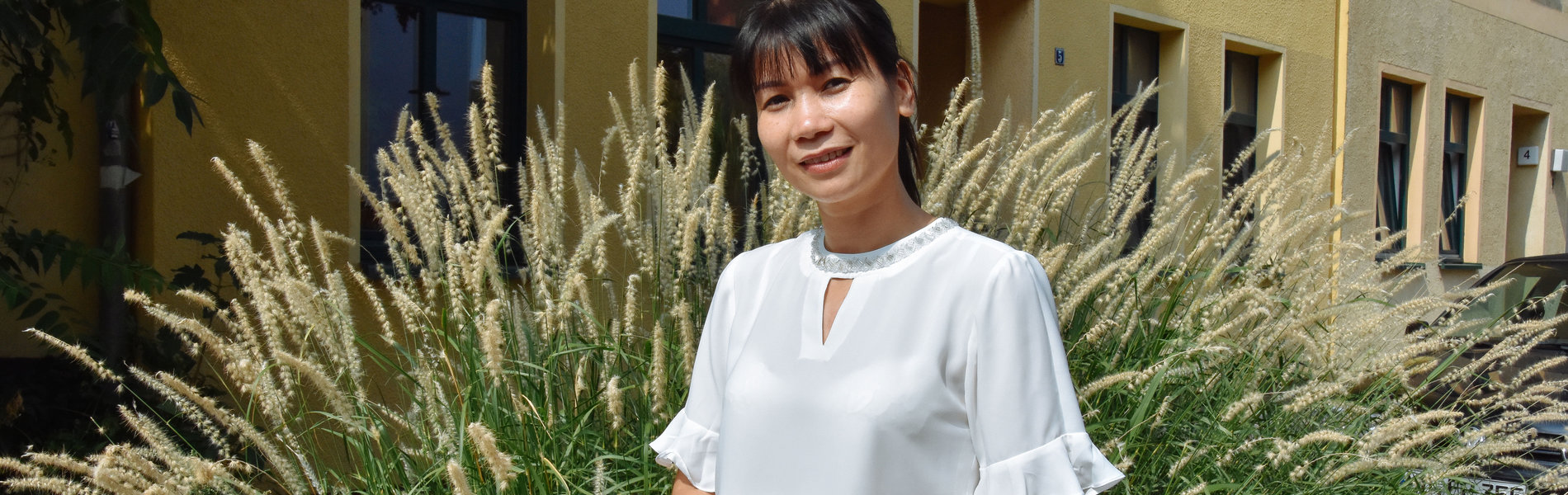 Eine schlanke Frau aus Vietnam lächelt freundlich in die Kamera. Sie trägt eine weiße Bluse und hat schwarze Haare.