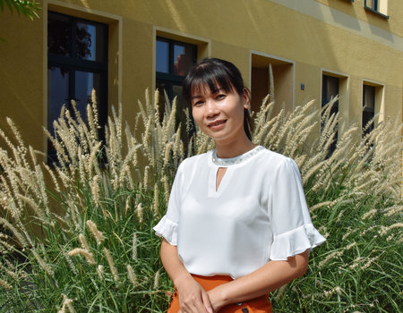 Eine schlanke Frau aus Vietnam lächelt freundlich in die Kamera. Sie trägt eine weiße Bluse und hat schwarze Haare.