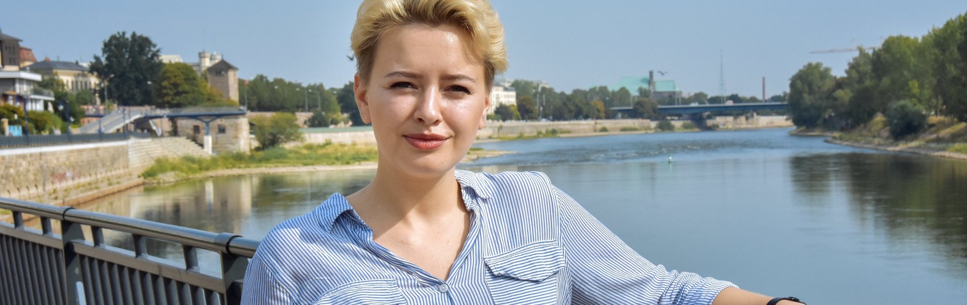 Eine junge blonde Frau steht an der Elbe.