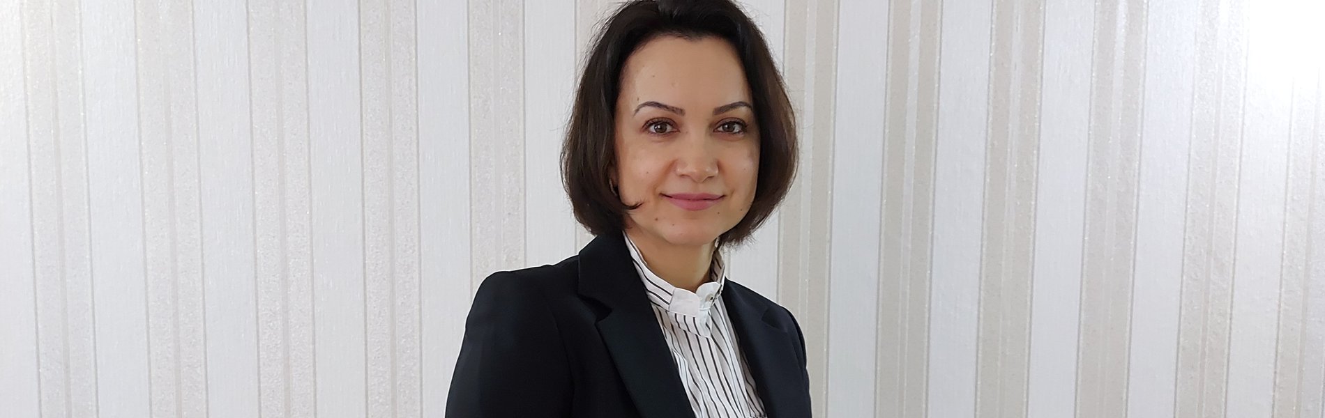 Eine junge Frau steht im Business-Outfit für einer Wand.