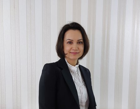 Eine junge Frau steht im Business-Outfit für einer Wand.