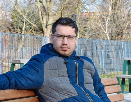 Ein junger Mann sitzt auf einer Bank und schaut ernst.
