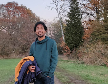 Ein junger Mann aus Indien steht auf einem Waldweg.