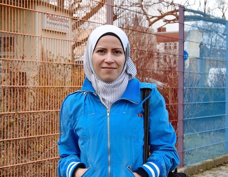 Eine junge Frau mit Kopftuch steht vor einem bunten Zaun