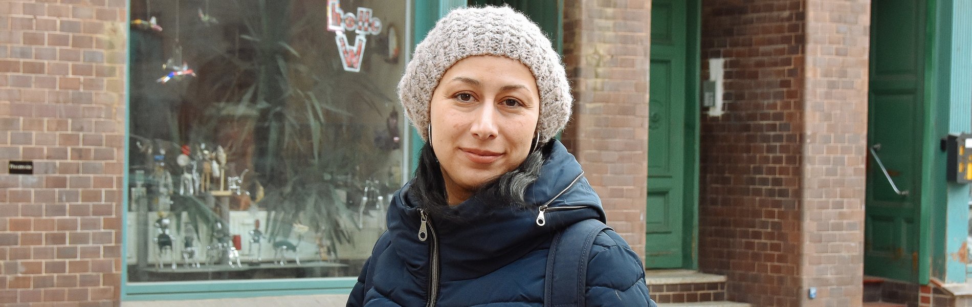 Eine junge Frau steht auf der Straße. Sie trägt eine dicke Jacke und eine Mütze.