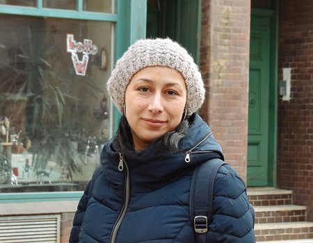 Eine junge Frau steht auf der Straße. Sie trägt eine dicke Jacke und eine Mütze.