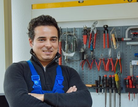 Ein junger Mann in Arbeitskleidung steht vor einer Werkbank.