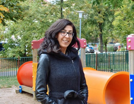 Eine junge Frau steht auf einem Kinderspielplatz. Sie lächelt. 