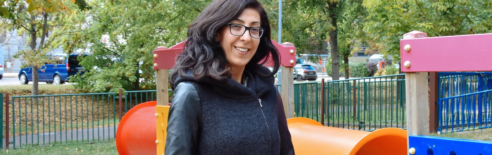 Eine junge Frau steht auf einem Kinderspielplatz. Sie lächelt.