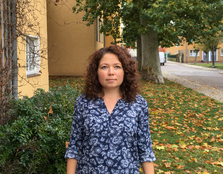 Eine junge Frau steht im Vorgarten ihres Hauses.