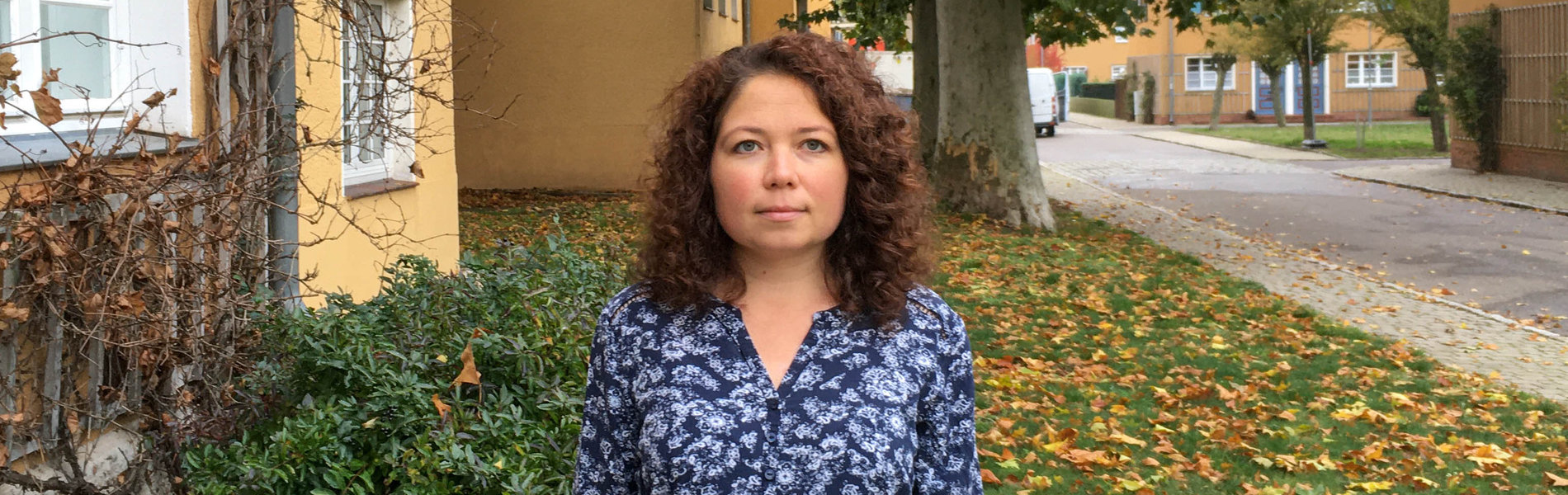 Eine junge Frau steht im Vorgarten ihres Hauses.