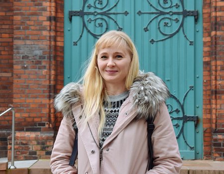Ein junge blonde Frau steht vor einer Kirche.