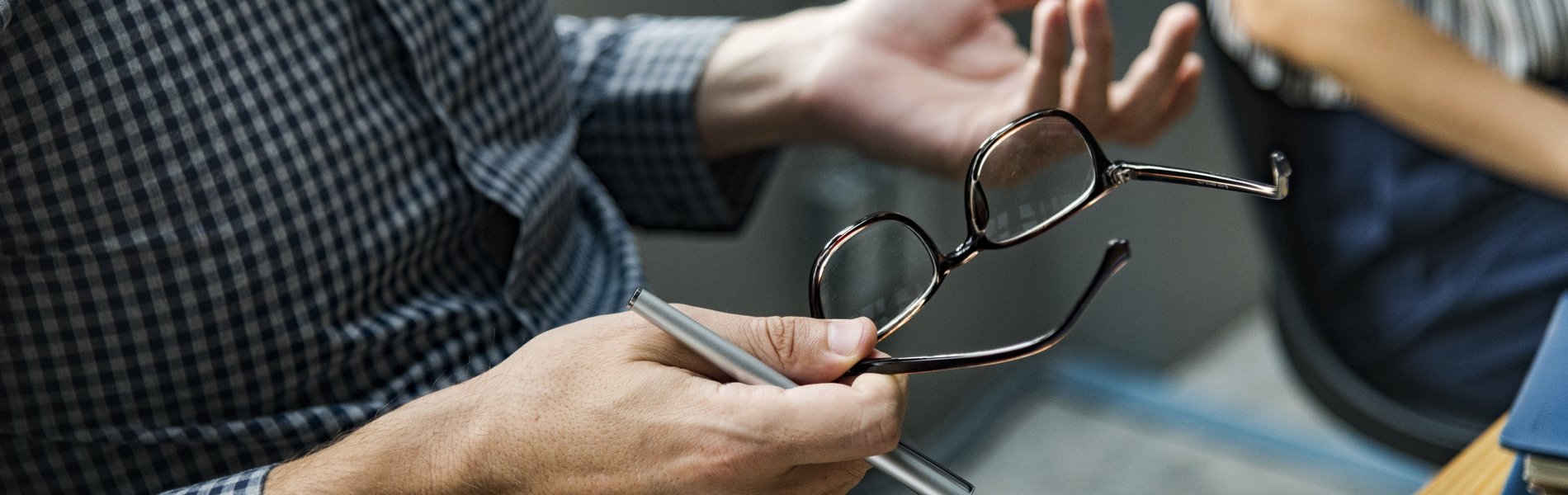 Das Foto zeigt eine Gesprächssituation in einer Fortbildung. Ein Mann in einem karierten Hemd gestikuliert beim Argumentieren mit den Händen. Dabei hat er seine BRille abgenommen und hält diese sowie einen Stift in seinen Händen.