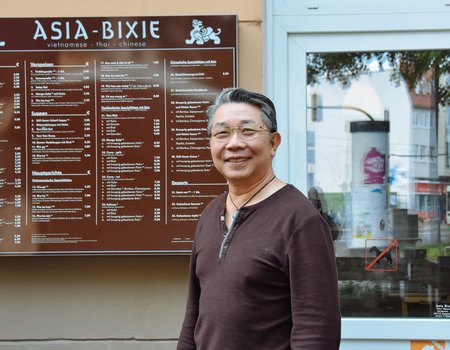 Ein ältere Mann steht vor seinem asiatischen Restaurant.