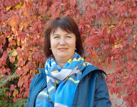 Eine Frau steht vor einer bewachsenen Häuserwand. Es ist Herbst und die Farben leuchten.