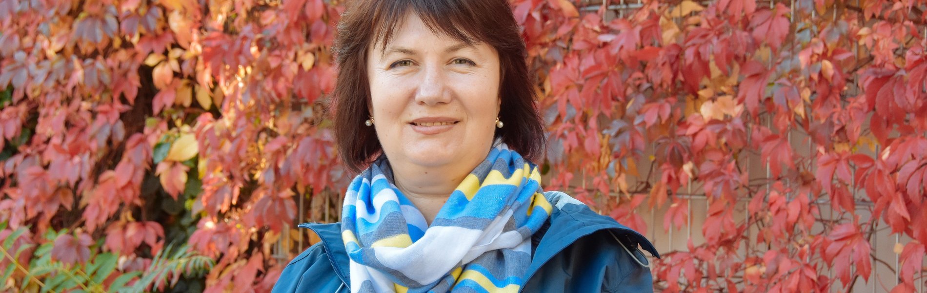 Eine Frau steht vor einer bewachsenen Häuserwand. Es ist Herbst und die Farben leuchten.