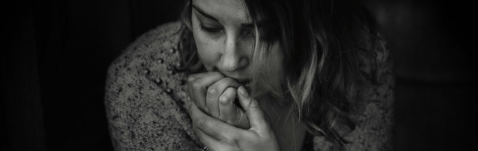 Das Foto ist in schwarz weiß. Es strahlt eine Melancholie und Verletzlichkeit aus. Eine Frau Ende 20 sitzt vor uns. Sie hat den Blick etwas zur Seite geneigt. Und schaut gedankenversunken auf den Boden. Ihr Kopf stützt sich etwas auf ihre Hände. Es scheint, als knabbere ihr Mund an den Fingern der rechten Hand. Aus Angst oder Verzweiflung.
