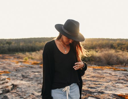 Eine junge Frau strägt einen großen Hut im Sonnenuntergang.